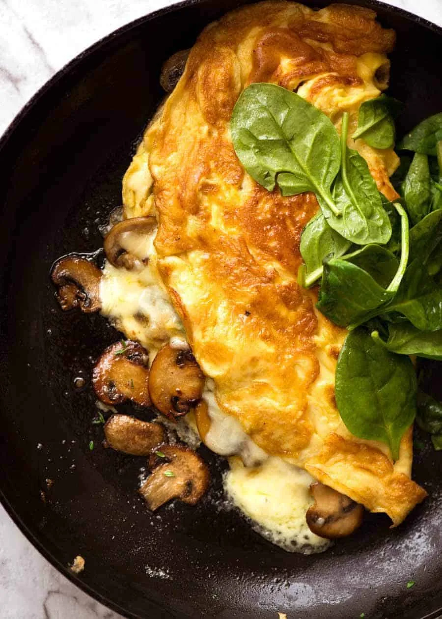 Folded omelette with mushrooms and melted cheese, served with fresh spinach