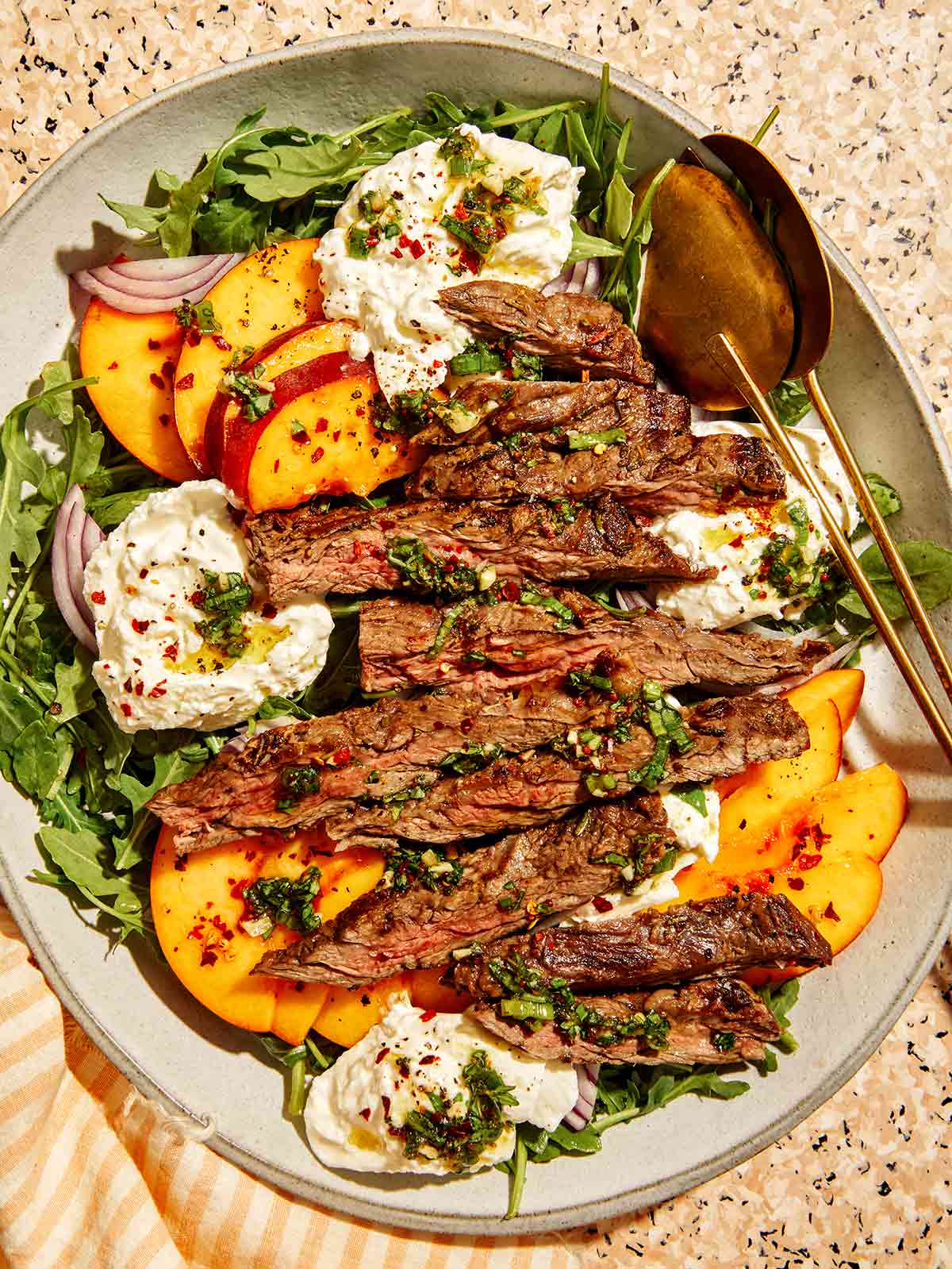 Sliced skirt steak over arugula with peaches, burrata, and herb chimichurri